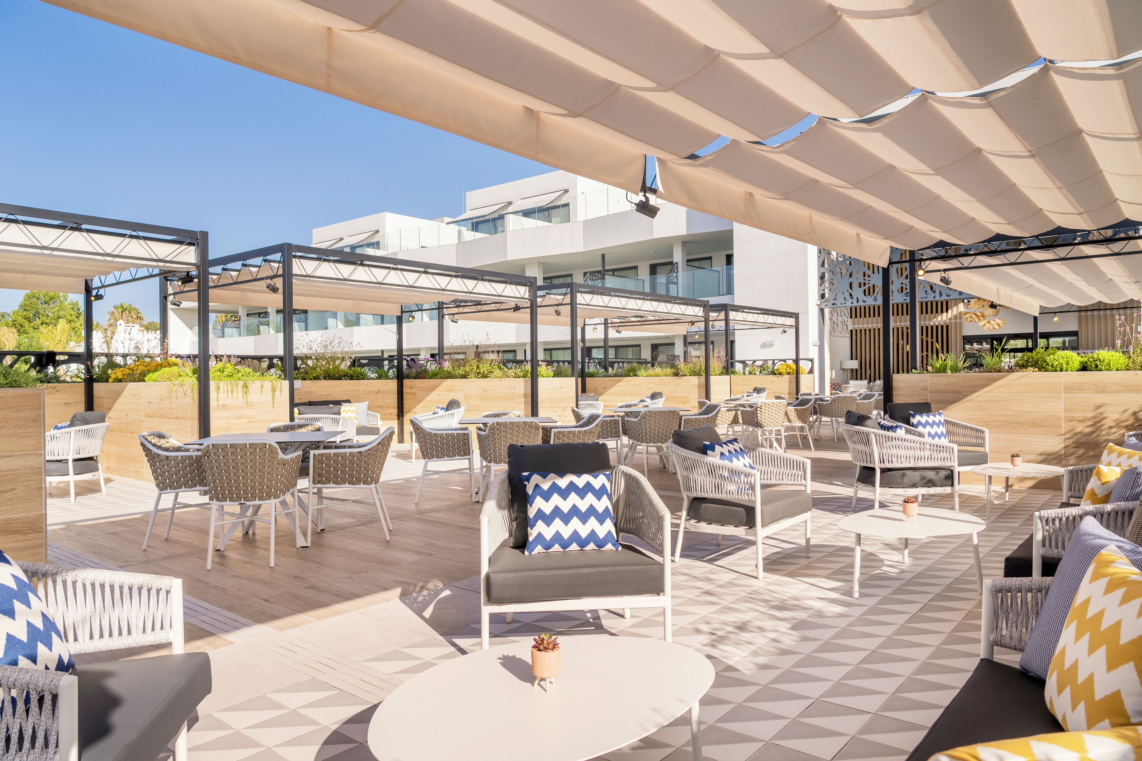 Un patio exterior con varias zonas de estar, incluyendo sofás y sillones, dispuestas bajo un amplio toldo.