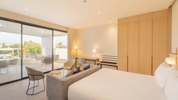 Habitación de hotel moderna con una cama grande, un sofá, un escritorio y una puerta de vidrio que da a una zona de estar al aire libre.