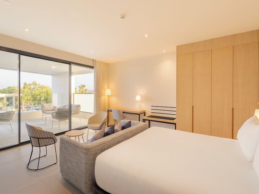 Habitación de hotel moderna con una cama grande, un sofá, un escritorio y una puerta de vidrio que da a una zona de estar al aire libre.