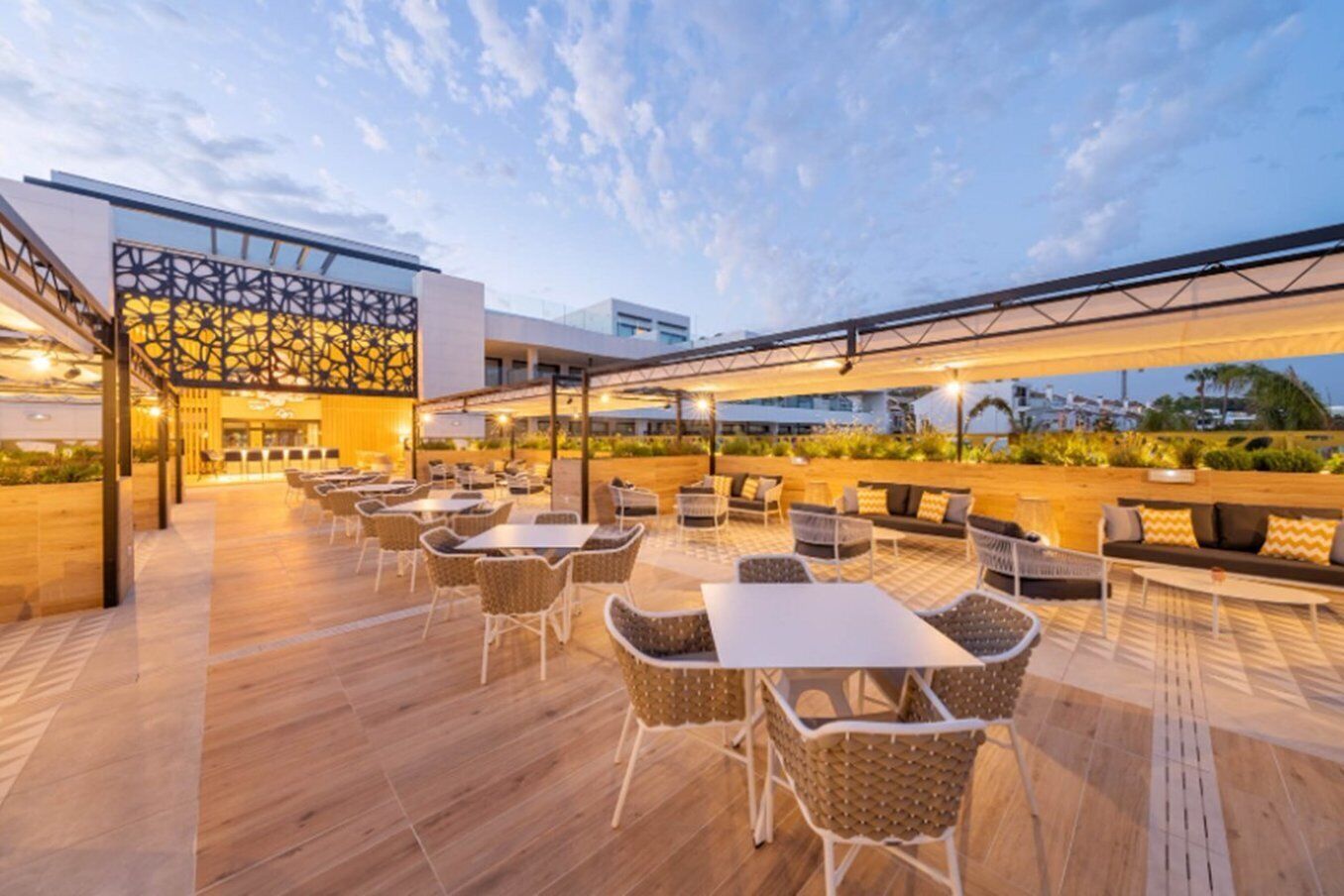 An outdoor seating area with tables and chairs, a wooden floor, and a decorative wall.