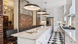 A modern kitchen with a large island, white cabinets, a black and white checkered floor, and a brick accent wall.