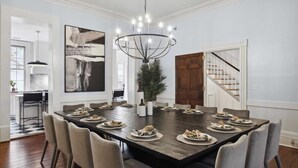 A dining room with a large rectangular table set for a meal, surrounded by chairs.