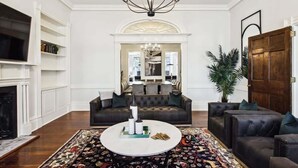A living room with a fireplace, a large round coffee table, and a chandelier.