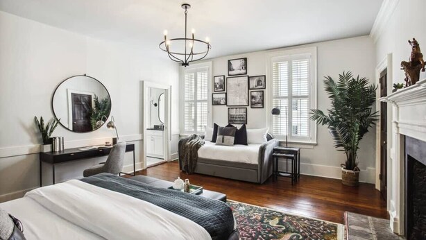 A bedroom with a bed, bedside table, mirror, dresser, and a fireplace.