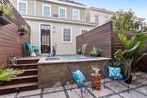 Un jardin avec un jacuzzi, deux chaises et une petite table sur laquelle sont posées des bouteilles.