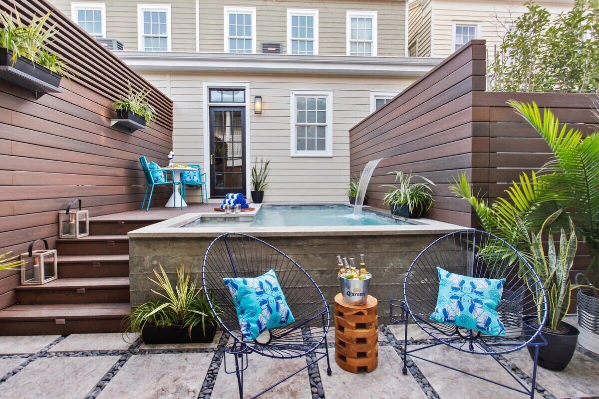 A backyard with a hot tub, two chairs, and a small table with bottles.