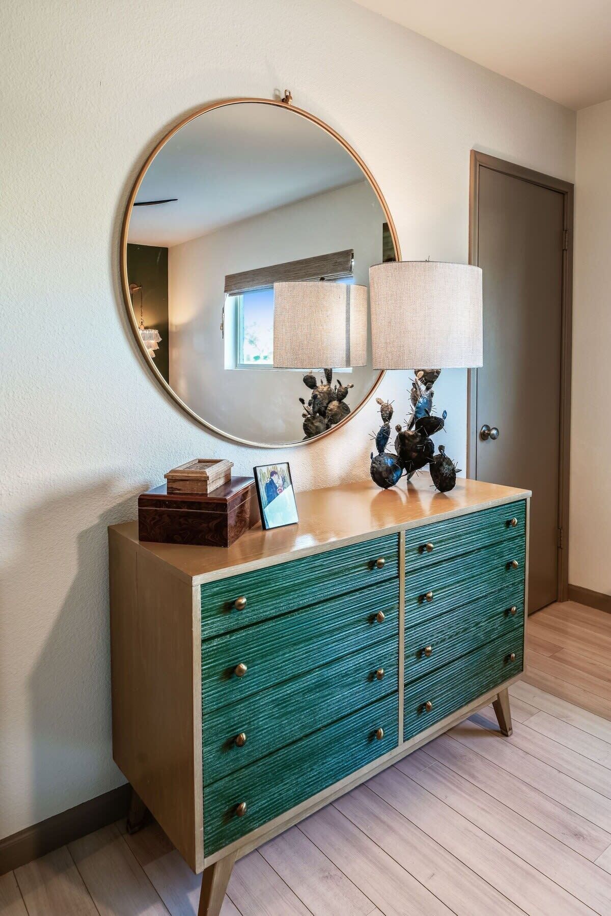 A room with a wooden dresser, a round mirror, and a lamp.