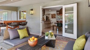 A modern living area with a sofa set, a coffee table with a bowl of oranges, and a dining area visible through an open door. - Glamorous Renovated Desert Oasis, Heated Pool, Tub (Scottsdale)