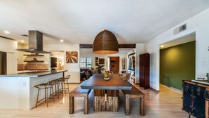 A modern kitchen with a central island, bar stools, and a large dining table. - Glamorous Renovated Desert Oasis, Heated Pool, Tub (Scottsdale)