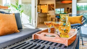 A modern living area with a sofa, a tray with glasses and a pitcher, and a dining area in the background. - Glamorous Renovated Desert Oasis, Heated Pool, Tub (Scottsdale)