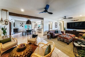 A spacious living room with wicker furniture, a large TV, and a ceiling fan.