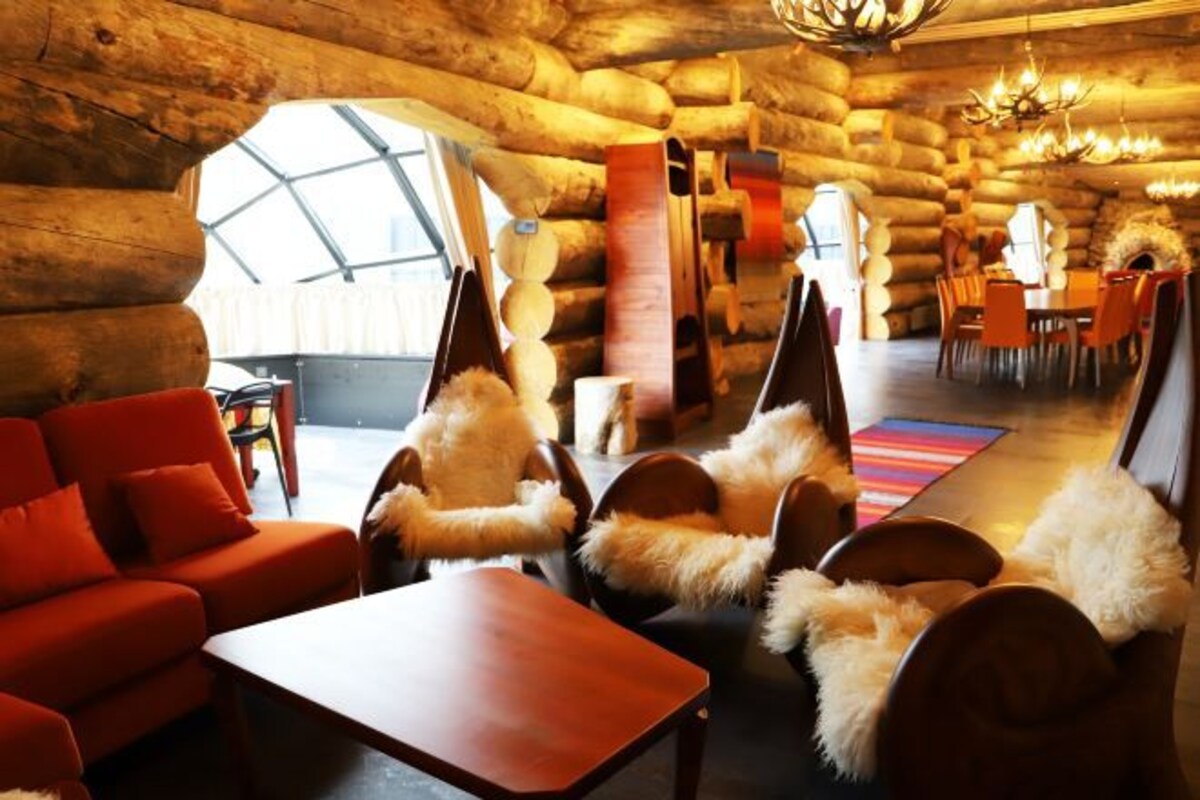 A log cabin interior with a dining area, a sofa, and chairs with fur throws.