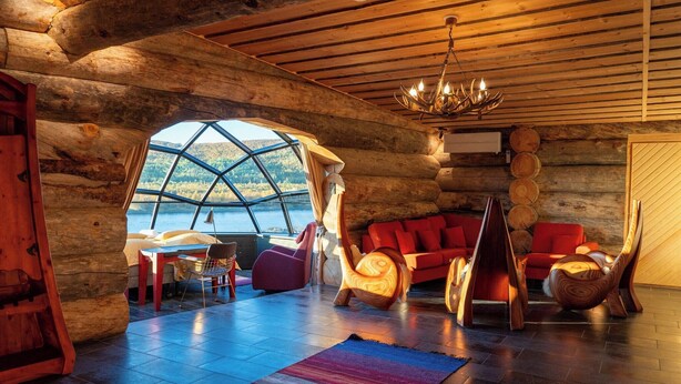 A log cabin interior with a large window, wooden furniture, and a chandelier. - Utsjoki Arctic Resort (Utsjoki)