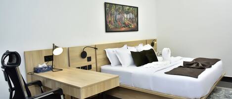 Quarto de hotel com cama, escrivaninha, cadeira e pintura na parede.