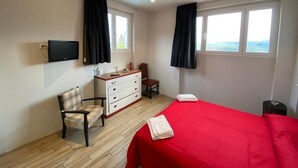 A bedroom with a red bedspread, a wooden dresser, a chair, a desk, and two windows with black curtains. - NiGiNo house sleeps 6, private pool and garden (Donnini)
