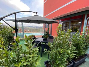 Un patio al aire libre con una mesa y sillas, rodeado de plantas en macetas y vistas a una piscina.
