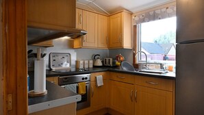 Ett kompakt kök med träskåp, ett kylskåp i rostfritt stål, en inbyggd ugn och ett fönster med utsikt över omgivningen.