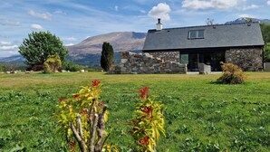 A stone house with a dark roof, surrounded by a grassy field and a mountain in the background. - The Barn in Banavie near Fort William (Fort William)