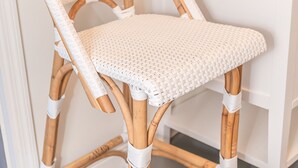 A wicker chair with a woven seat and backrest, positioned in front of a white vanity with a gold faucet and a mirror above it. - Cozy cottage close to downtown Hayesville (Hayesville)