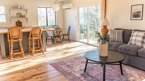 A spacious living area with a wooden floor, a gray sofa, a round coffee table, and a dining area with wicker chairs and a wooden table. - Cozy cottage close to downtown Hayesville (Hayesville)