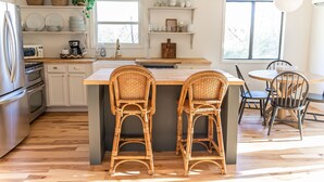A kitchen with a central island, two wicker bar stools, a dining table with chairs, and a refrigerator. - Cozy cottage close to downtown Hayesville (Hayesville)