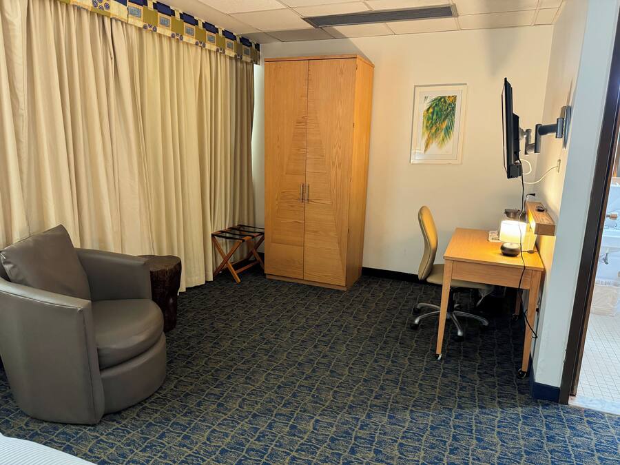 A hotel room with a bed, a desk, a chair, a wardrobe, and a small table.