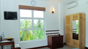 A room with a large window, a TV mounted on the wall, a wooden wardrobe, a desk with a chair, and a bed with a blue bedspread. - Antares Dhangethi (Dhangethi)