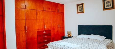 Un dormitorio con un amplio armario de madera, una cama con colcha estampada y dos cuadros en la pared.