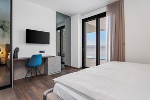 A hotel room with a bed, a desk with a chair, a television, and a sliding glass door leading to a balcony with a view.