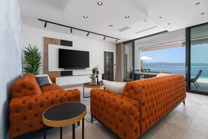 A modern living room with a large sofa, a television, and a view of the sea.