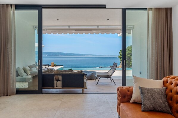 A modern living room with a large sliding glass door leading to a balcony with a view of the sea.