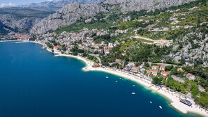Vue aérienne d’une ville côtière, avec une plage, des bâtiments et des montagnes en arrière-plan.