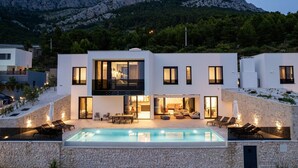 Une maison moderne à deux étages, dotée d’une piscine, d’un espace extérieur aménagé et offrant une vue sur les montagnes.