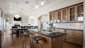 A spacious kitchen with wooden cabinets, a central island with bar stools, pendant lighting, and a fireplace. - Beach Front Cottage with Beautiful Ocean Views! (Crystal Beach)