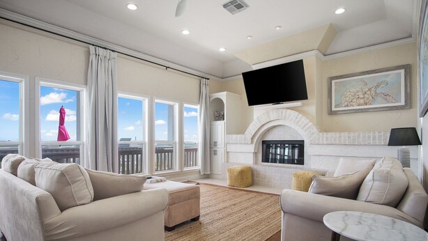 A spacious living room with a fireplace, large windows, and a flat-screen TV. - Beach Front Cottage with Beautiful Ocean Views! (Crystal Beach)