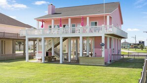 A pink two-story building with a balcony, outdoor seating, and a staircase. - Beach Front Cottage with Beautiful Ocean Views! (Crystal Beach)