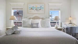 A neatly arranged bedroom with a large bed, two bedside tables, a desk, and a painting above the bed. - Beach Front Cottage with Beautiful Ocean Views! (Crystal Beach)