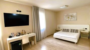 Une chambre d’hôtel avec un lit, un bureau équipé d’un ordinateur, une télévision et une petite poubelle.