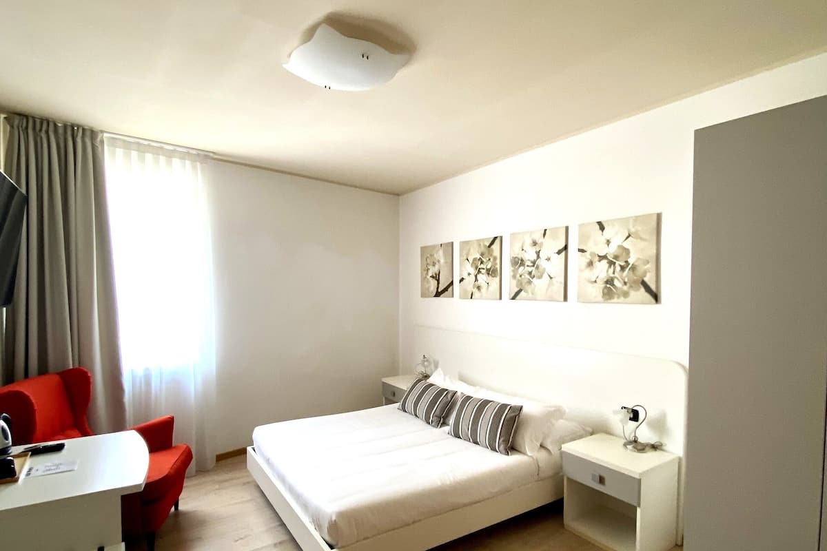 A modern hotel room with a bed, a desk, a chair, and a nightstand.