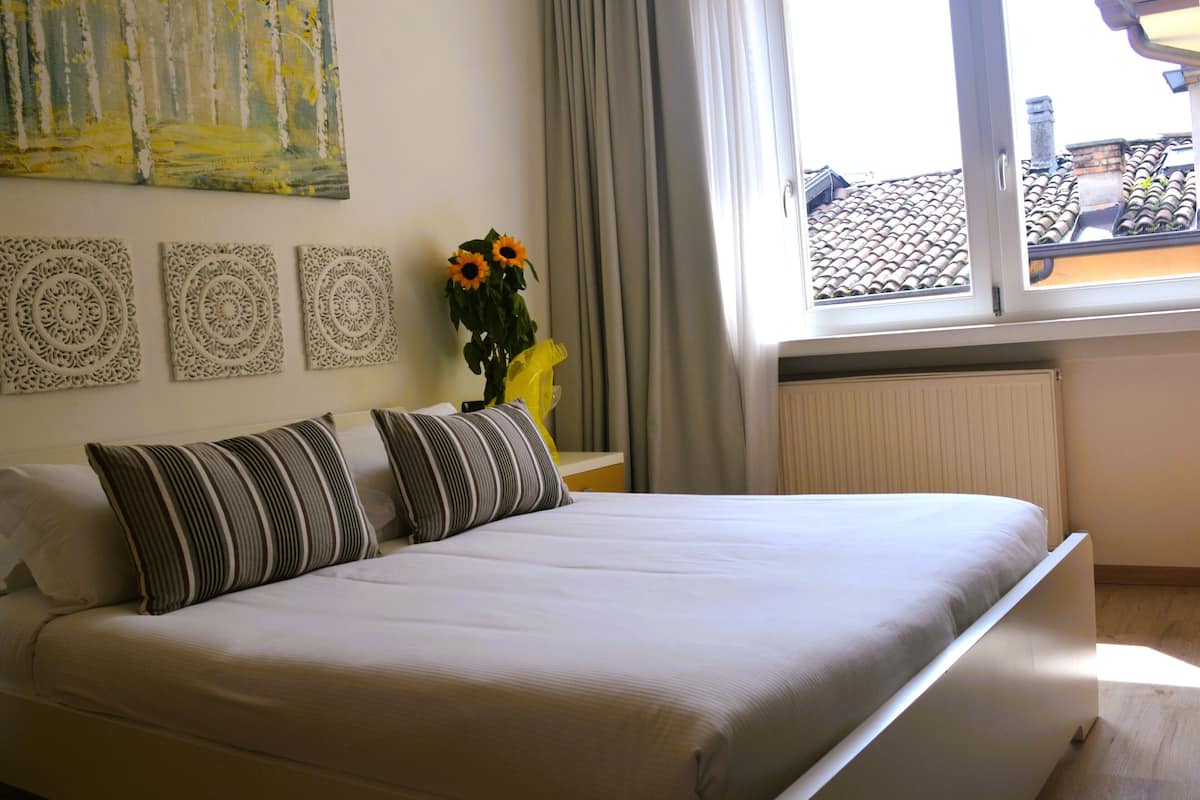 A neatly made bed with striped pillows, a vase with sunflowers, and a painting on the wall.