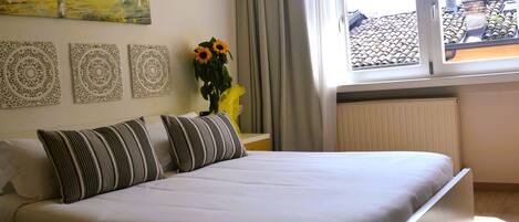 Ein ordentlich bezogenes Bett mit gestreiften Kissen, eine Vase mit Sonnenblumen und ein Bild an der Wand.