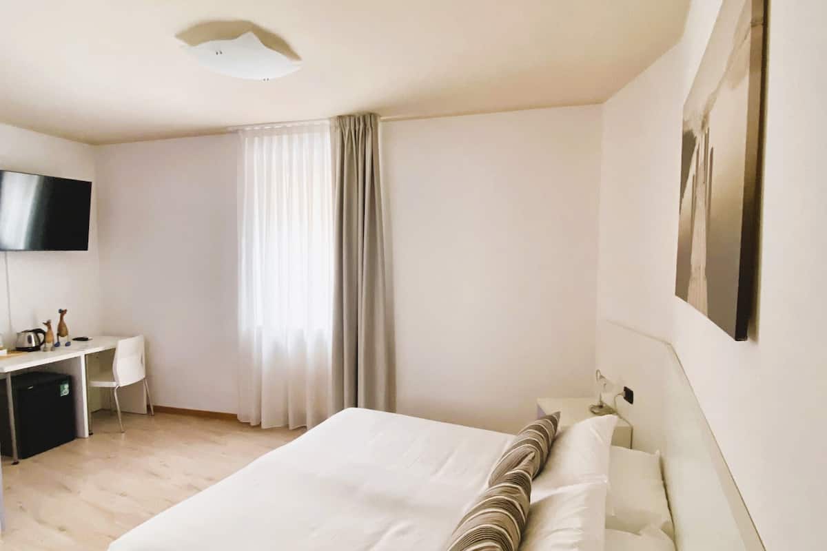 A hotel room with a large bed, a desk, a chair, a television, and a window with curtains.