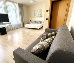 Una sala moderna con un sofá gris, una cama blanca y un televisor sobre un mueble.