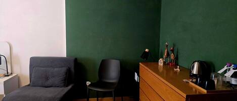 Una stanza con una parete verde, una scrivania in legno con un bollitore, una sedia e un divano.