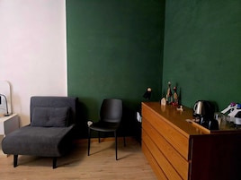 Una habitación con una pared verde, un escritorio de madera con un hervidor, una silla y un sofá.