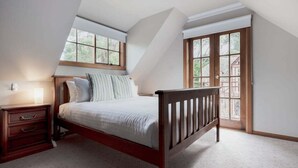 A bedroom with a sloped ceiling, a wooden bed frame, a nightstand, and a window with a view of greenery. - Gracelands: Swiss Inspired Home (Blackstone Heights)