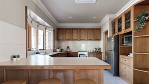 A modern kitchen with a large island, wooden cabinets, stainless steel appliances, and a view of the outdoors. - Gracelands: Swiss Inspired Home (Blackstone Heights)
