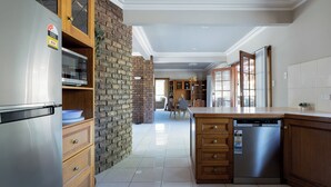 A modern kitchen with a stainless steel refrigerator, built-in microwave, and dishwasher. It features a brick accent wall and wooden cabinetry. - Gracelands: Swiss Inspired Home (Blackstone Heights)