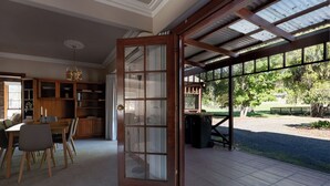 A spacious open-plan living area with a dining table, kitchen cabinets, and a large sliding glass door leading to an outdoor patio. - Gracelands: Swiss Inspired Home (Blackstone Heights)