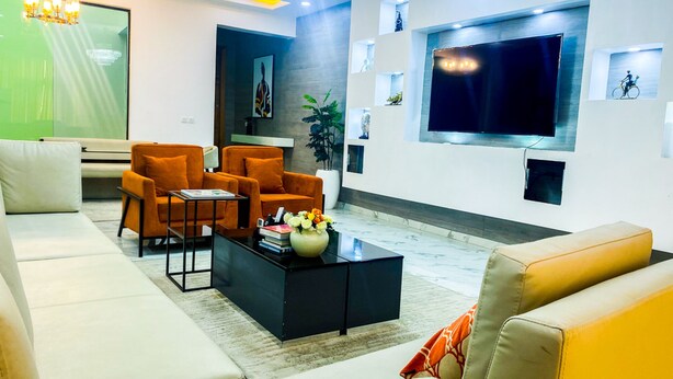 A modern living room with a large flat-screen TV, orange armchairs, a black coffee table, and a beige sofa. - Impeccable 2-bed Apartment in Lekki With Snooker (Lekki)